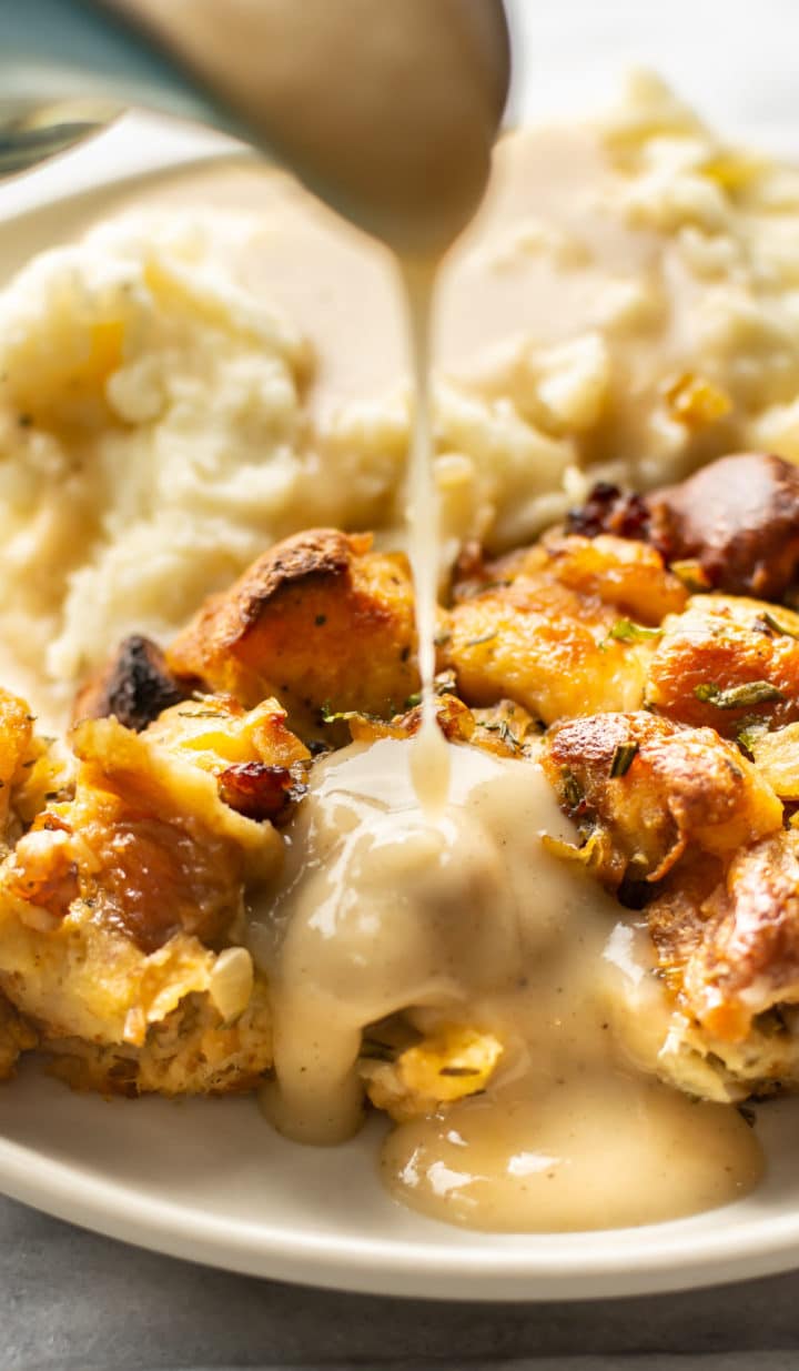 close-up of gravy being poured over stuffing on a plate with mashed potatoes in the background