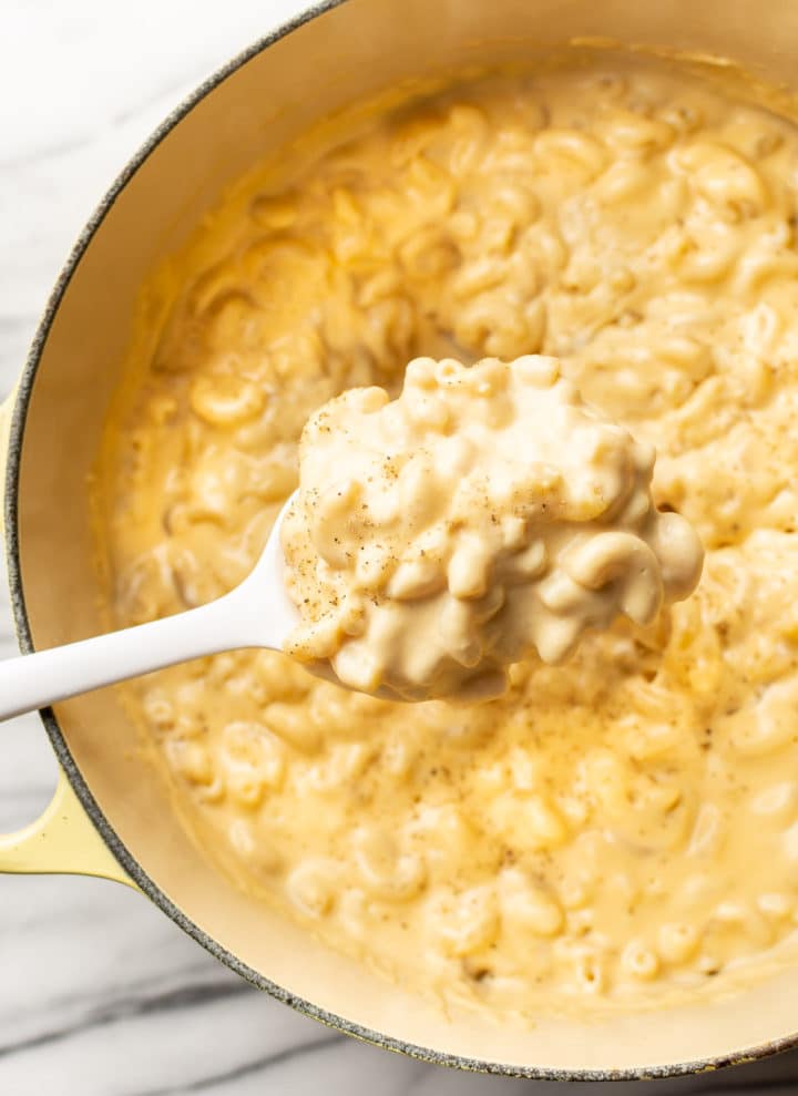 a large spoonful of creamy stovetop mac and cheese being scooped out of a yellow pot