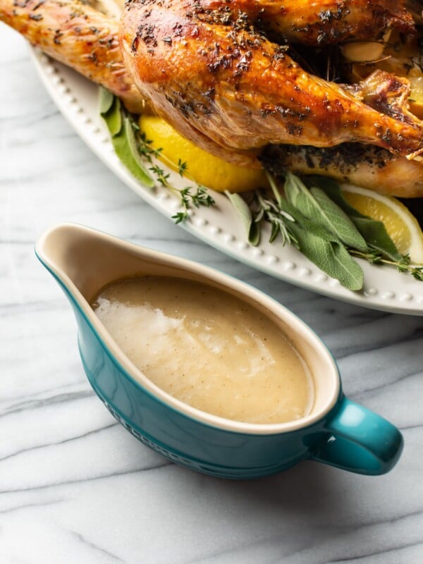 homemade turkey gravy in blue gravy boat with a roasted turkey in the background