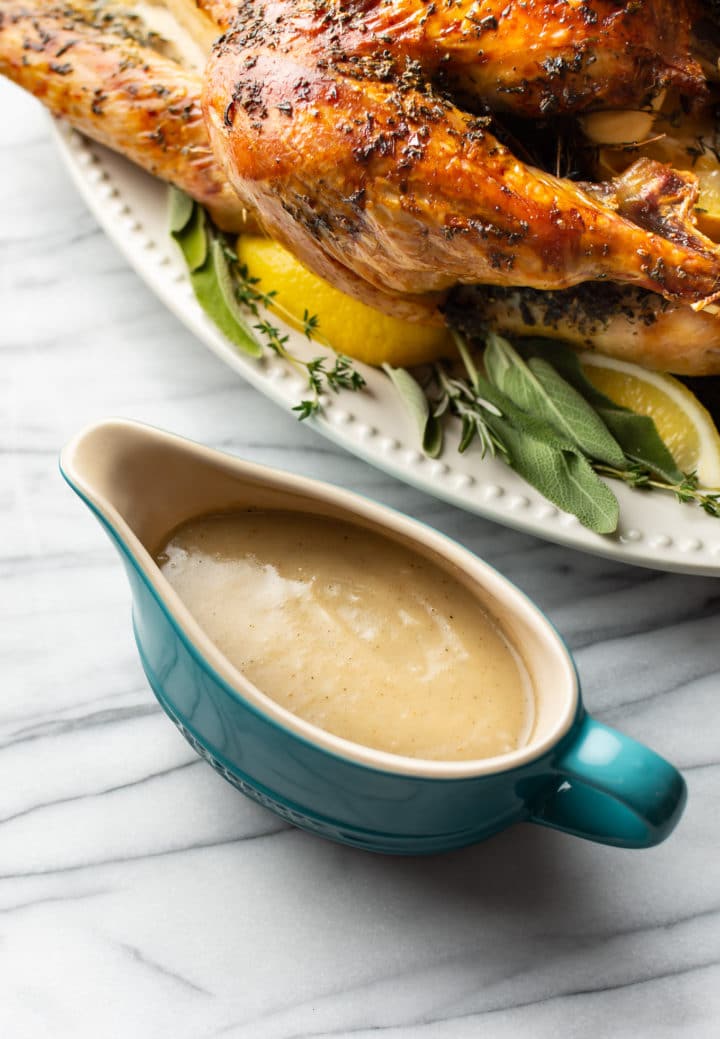 homemade turkey gravy in blue gravy boat with a roasted turkey in the background