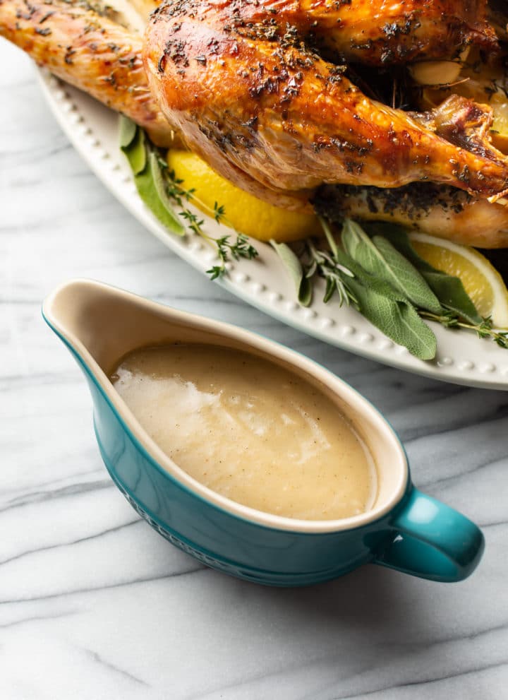 homemade turkey gravy in blue gravy boat with a roasted turkey in the background