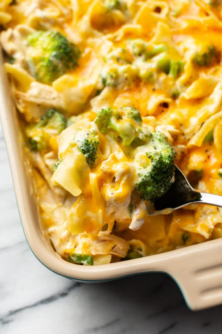 close-up of a serving spoon taking a large spoonful of chicken noodle casserole from the baking dish