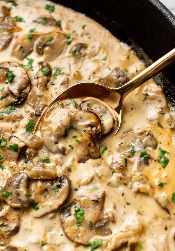 extreme close-up of creamy mushroom sauce in a cast iron skillet with a serving spoon