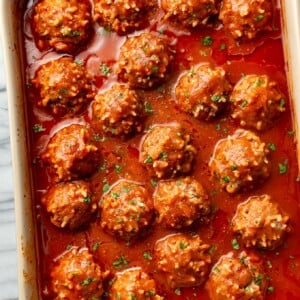 baking dish on marble surface with several porcupine meatballs in sauce