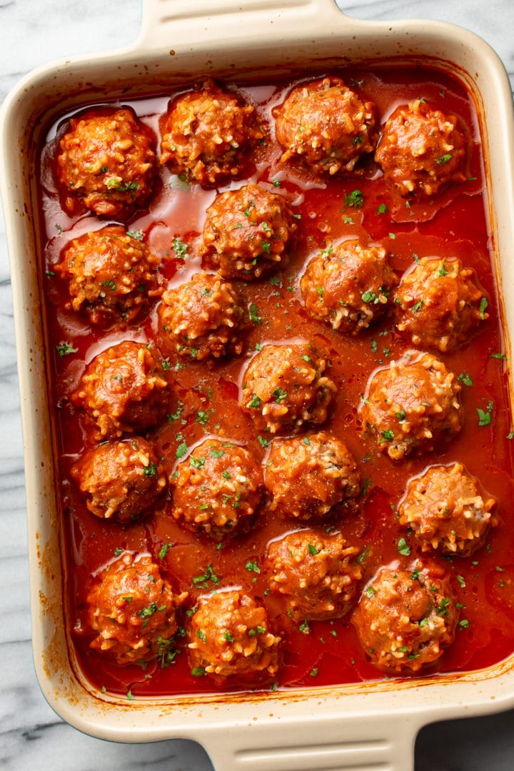 baking dish on marble surface with several porcupine meatballs in sauce