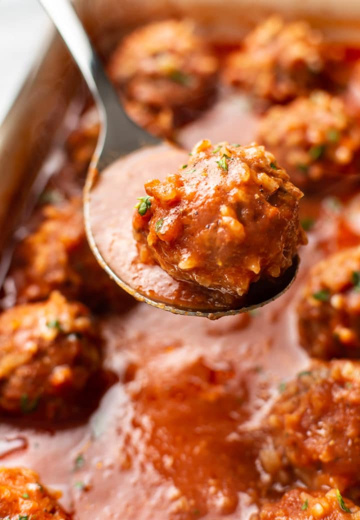 close-up of a meatball on a spoon with a baking dish full of baked porcupine meatballs in the background