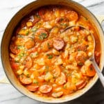 a large pot of sausage stew with a metal ladle