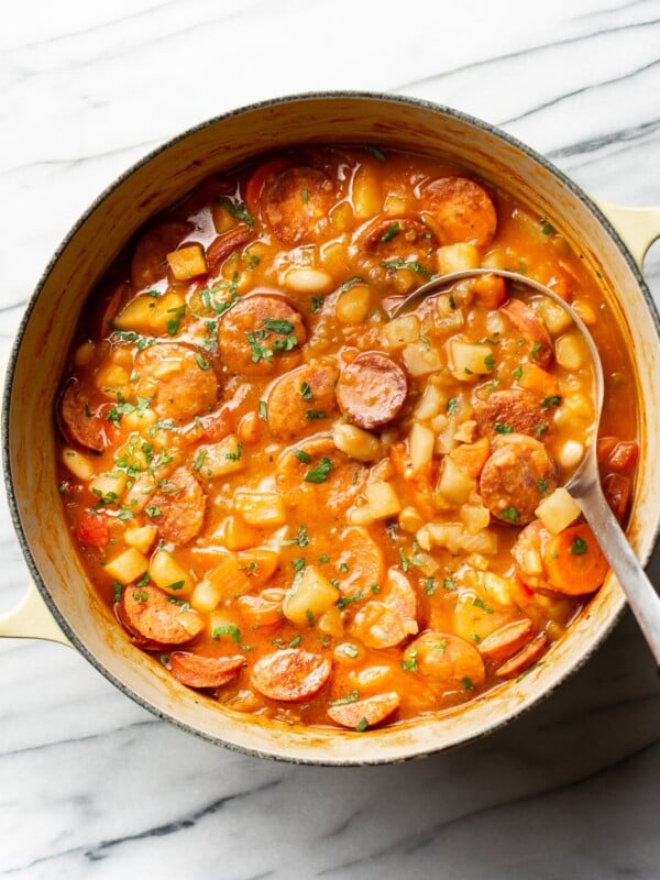 a large pot of sausage stew with a metal ladle