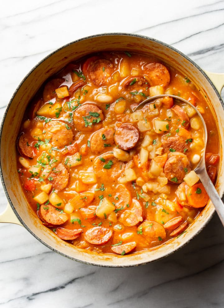 a large pot of sausage stew with a metal ladle