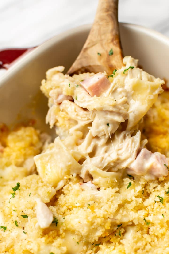 close-up a wooden spoon serving chicken cordon bleu casserole from a baking dish