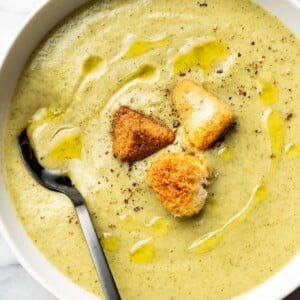 a bowl of cream of broccoli soup with croutons and a spoon