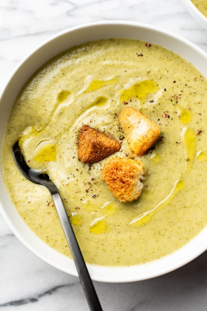 a bowl of cream of broccoli soup with croutons and a spoon