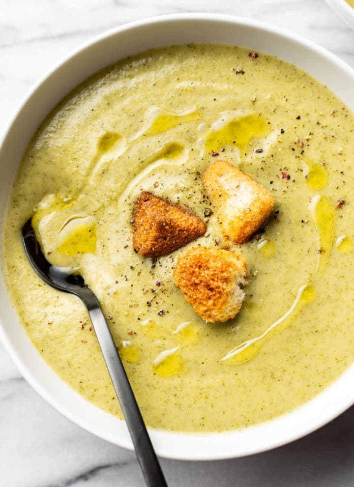 a bowl of cream of broccoli soup with croutons and a spoon