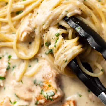 extreme close-up of serving tongs twirling creamy salmon spaghetti