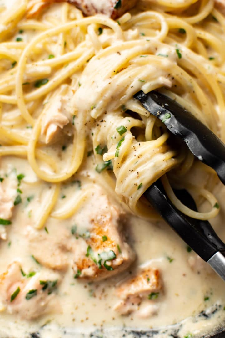 extreme close-up of serving tongs twirling creamy salmon spaghetti