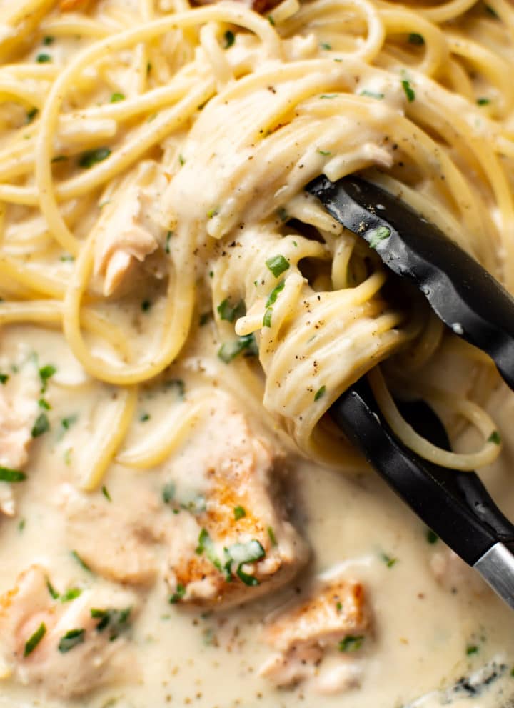 extreme close-up of serving tongs twirling creamy salmon spaghetti