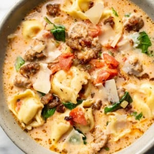 close-up of a bowl of italian sausage tortellini soup with shaved parmesan cheese on top