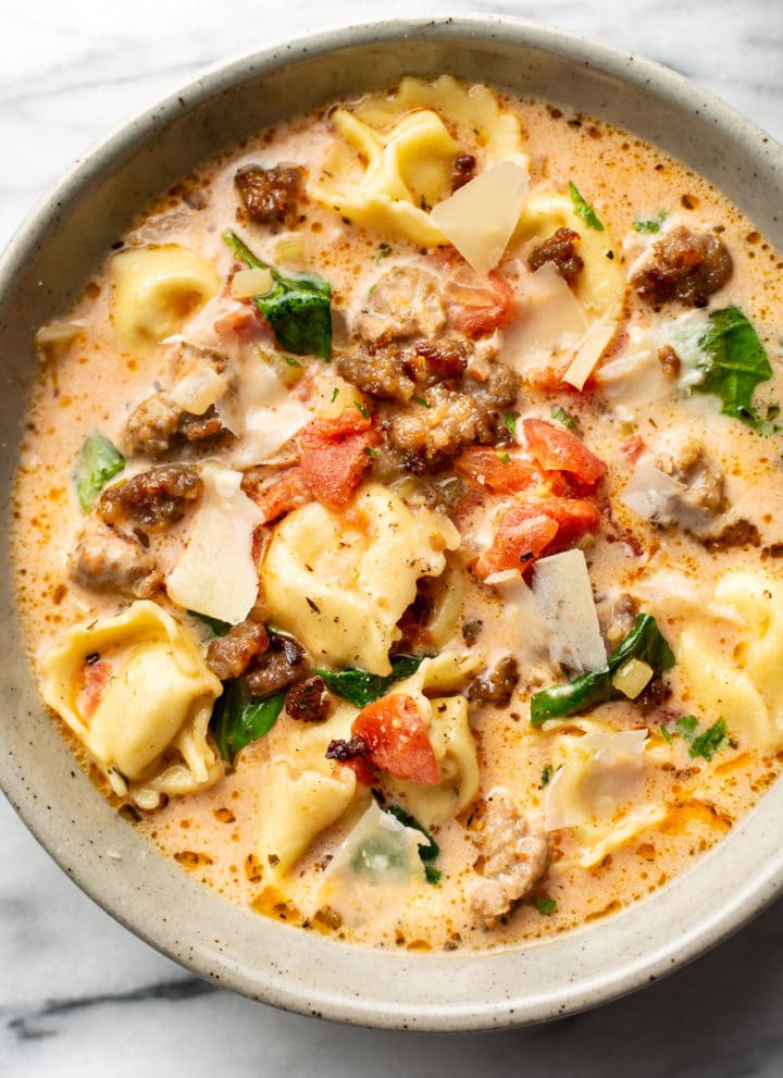 close-up of a bowl of italian sausage tortellini soup with shaved parmesan cheese on top