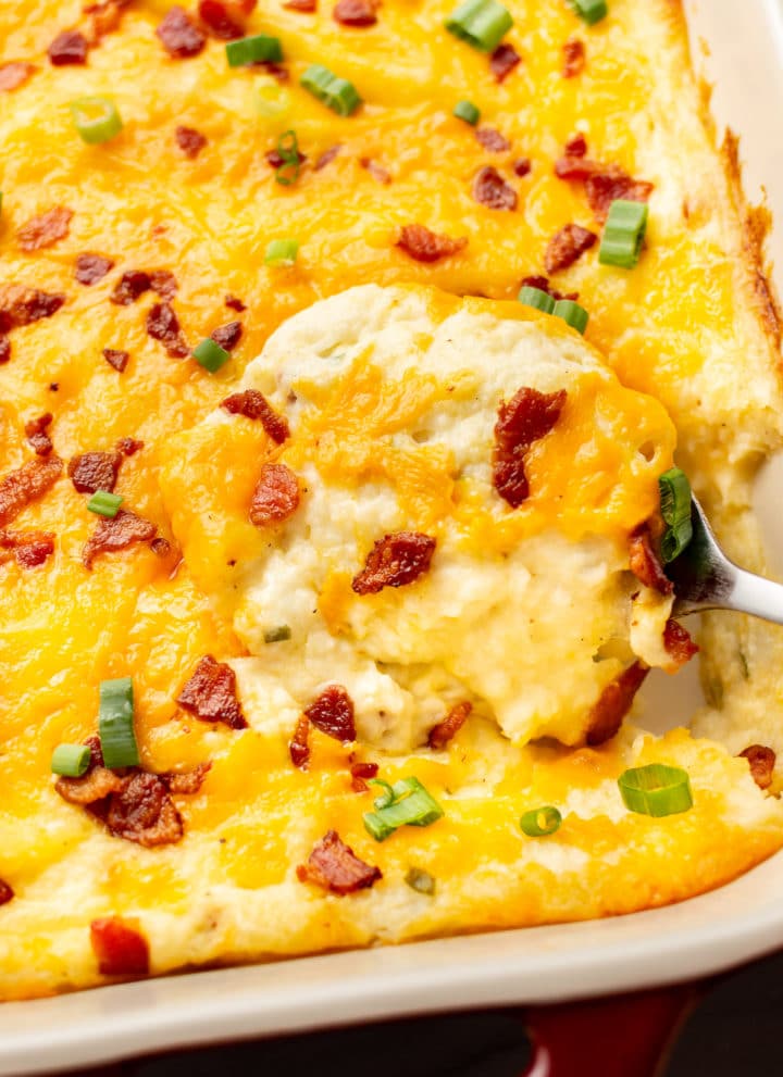 close-up of a serving spoon in a baking dish with loaded mashed potato casserole