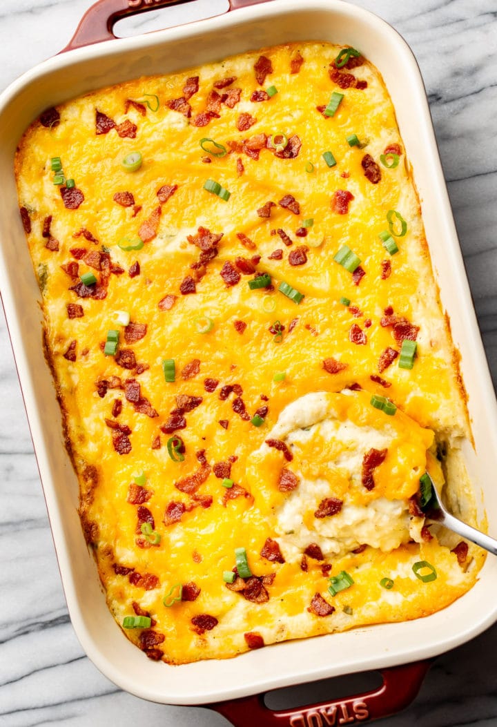 a baking dish with cheesy loaded mashed potato casserole and a serving spoon