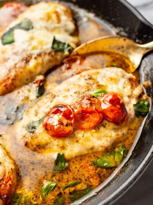 close-up of a spoon serving a portion of pesto chicken from a cast iron skillet