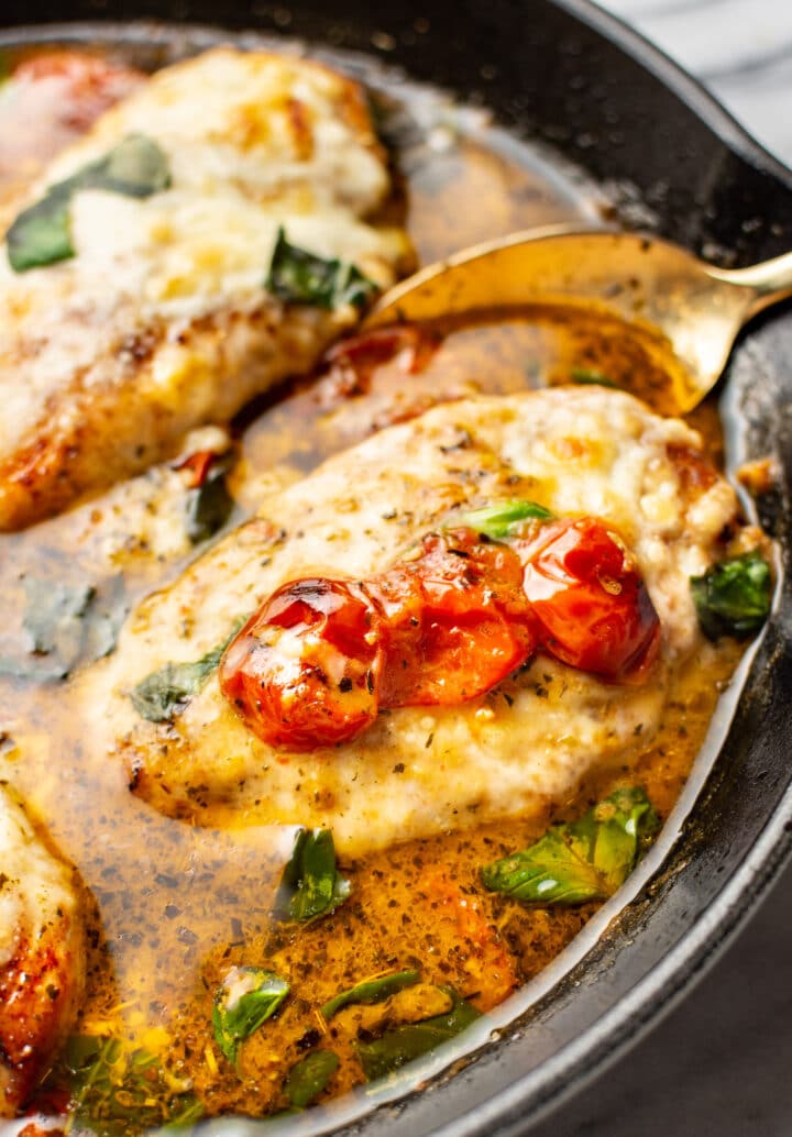 close-up of a spoon serving a portion of pesto chicken from a cast iron skillet