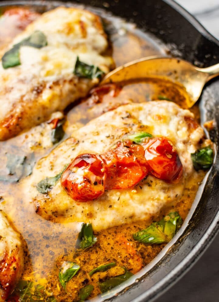 close-up of a spoon serving a portion of pesto chicken from a cast iron skillet