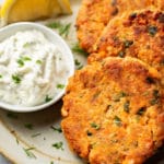 a plate with three salmon patties, a lemon wedge, and dip