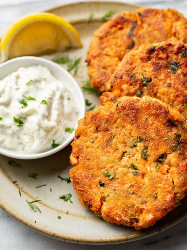 a plate with three salmon patties, a lemon wedge, and dip