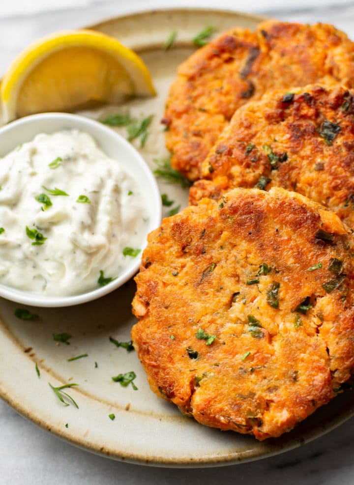 a plate with three salmon patties, a lemon wedge, and dip