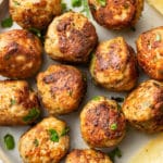 close-up of several ground turkey meatballs on a plate with lemon wedges