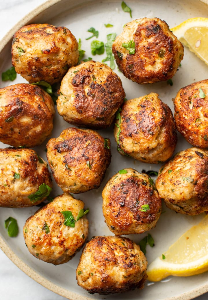 close-up of several ground turkey meatballs on a plate with lemon wedges