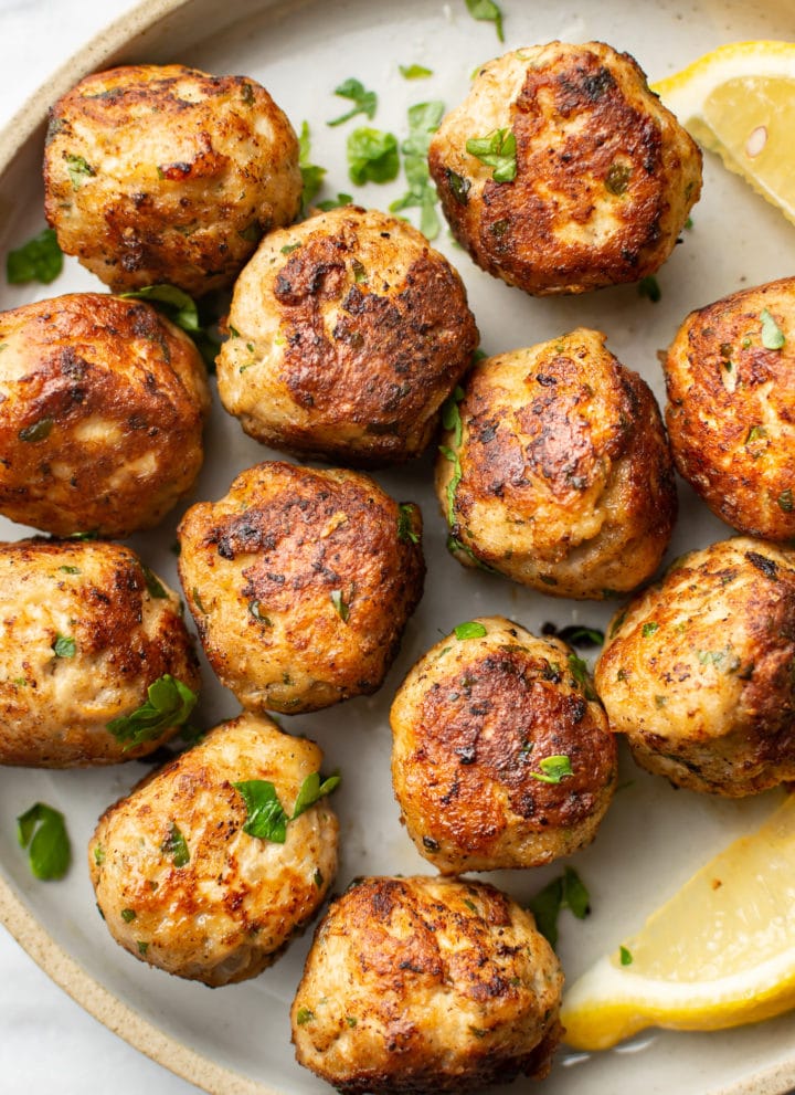 close-up of several ground turkey meatballs on a plate with lemon wedges