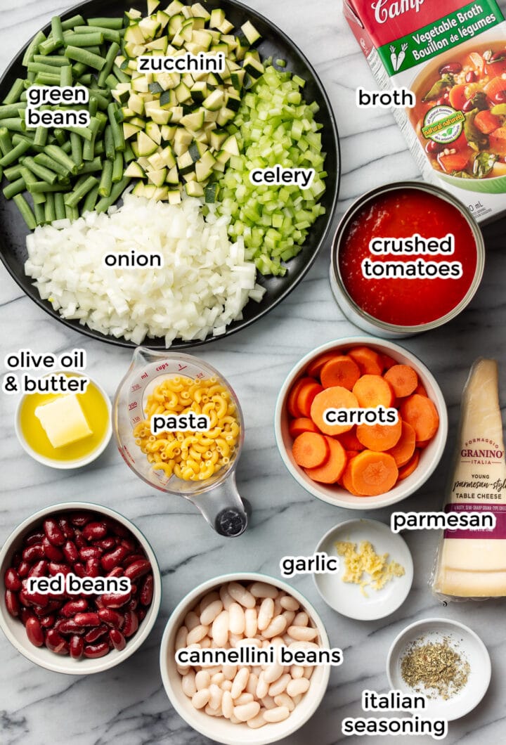 several bowls and plates on a marble surface with ingredients for making minestrone soup