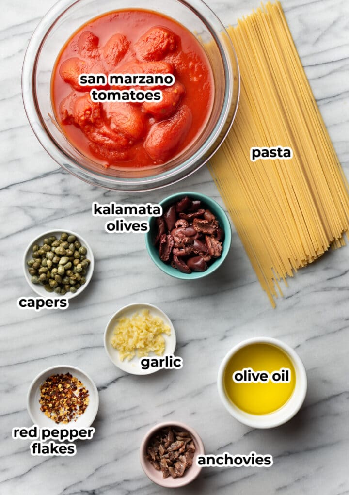 ingredients on a marble surface for pasta puttanesca