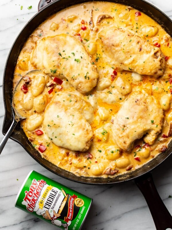 a cast iron skillet with cajun chicken and gnocchi next to a jar of tony chachere seasoning