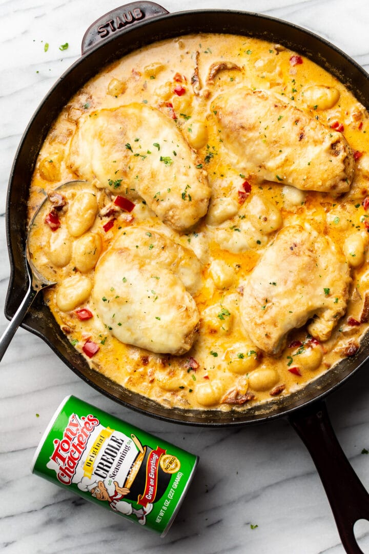 a cast iron skillet with cajun chicken and gnocchi next to a jar of tony chachere seasoning