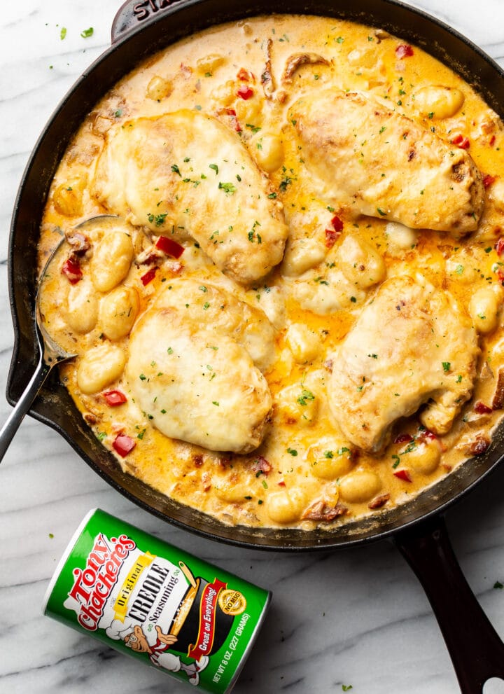 a cast iron skillet with cajun chicken and gnocchi next to a jar of tony chachere seasoning