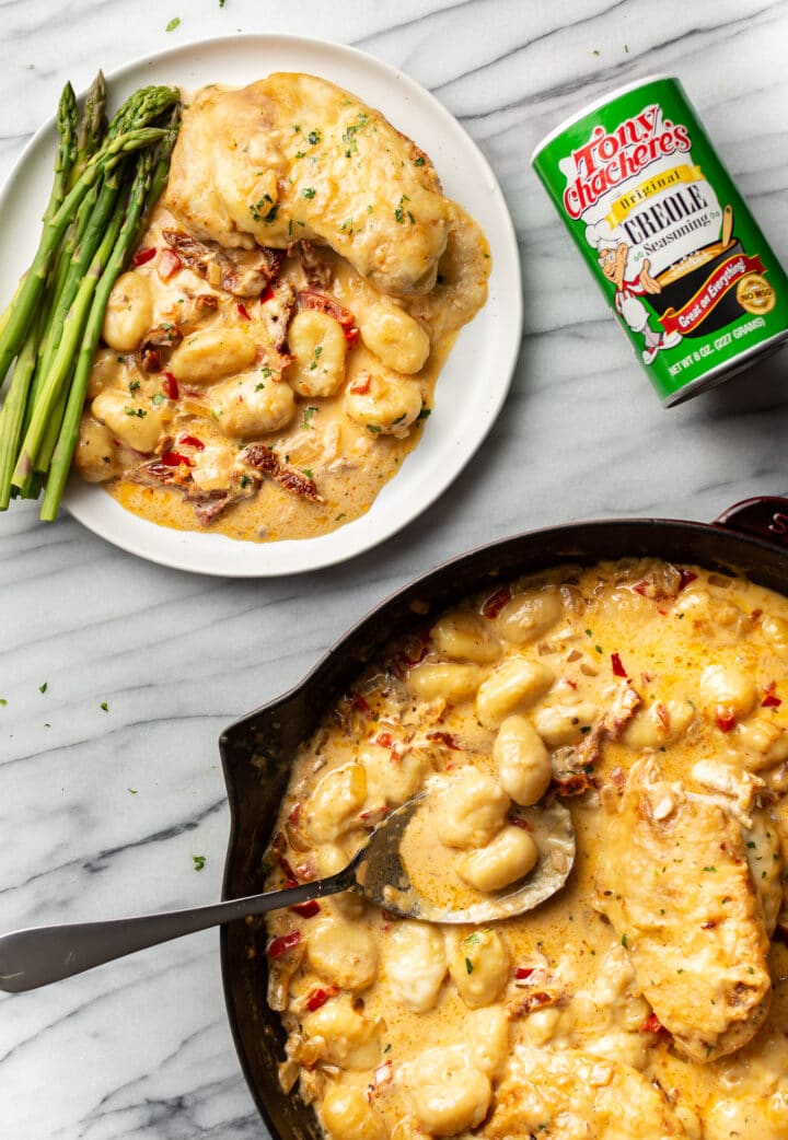 a skillet with cajun baked gnocchi next to a plate of it with asparagus next to a container of tony chachere's seasoning