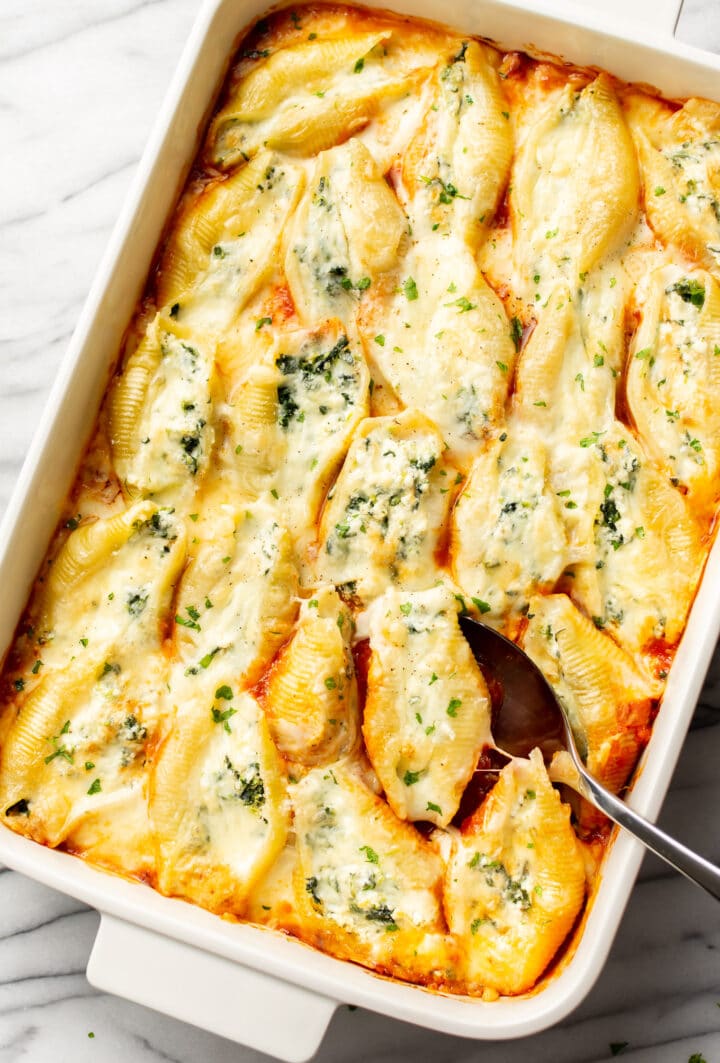 a casserole dish with stuffed shells and a serving spoon