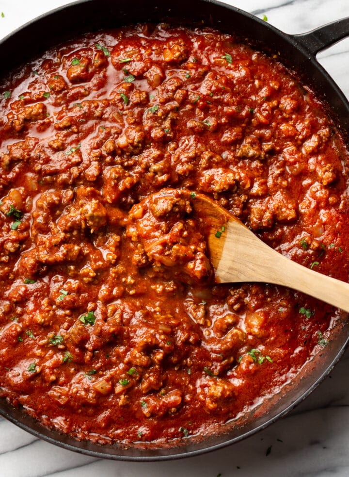 a wooden spoon in a skillet with meat sauce for spaghetti
