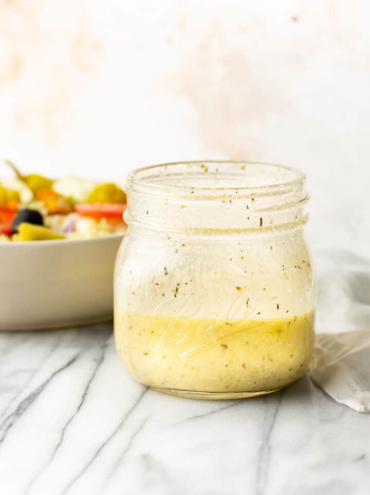 a jar of italian dressing next to a salad