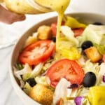 a jar of italian dressing being drizzled on a salad