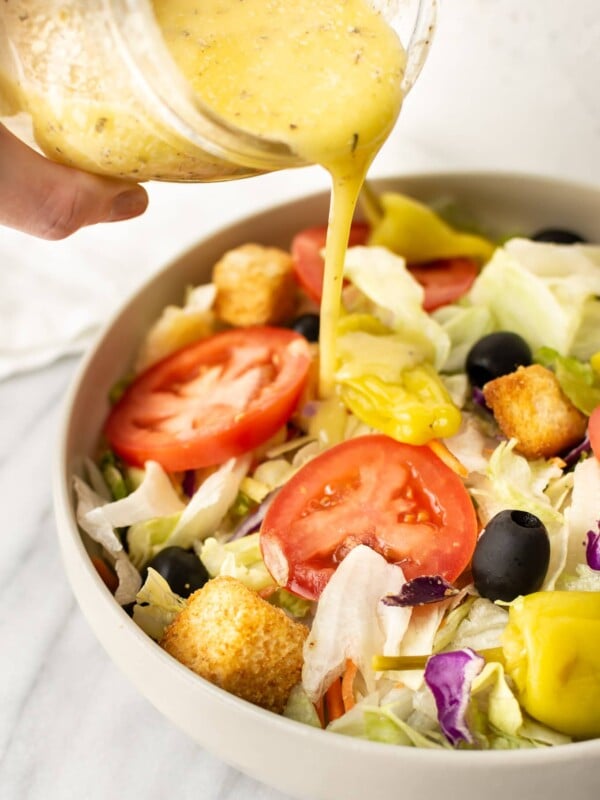 a jar of italian dressing being drizzled on a salad