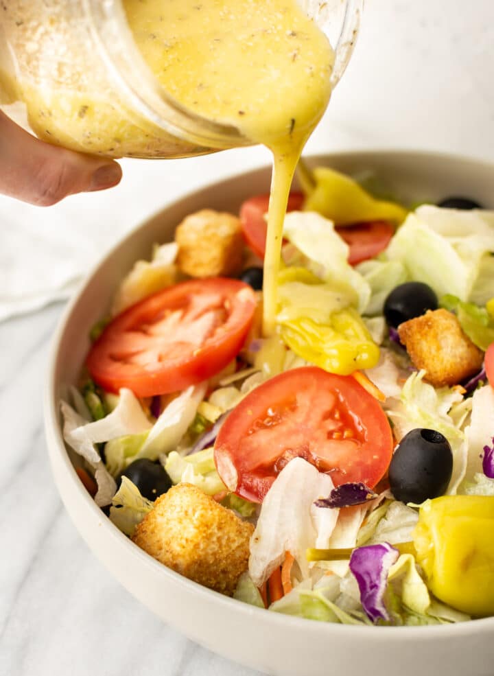 a jar of italian dressing being drizzled on a salad