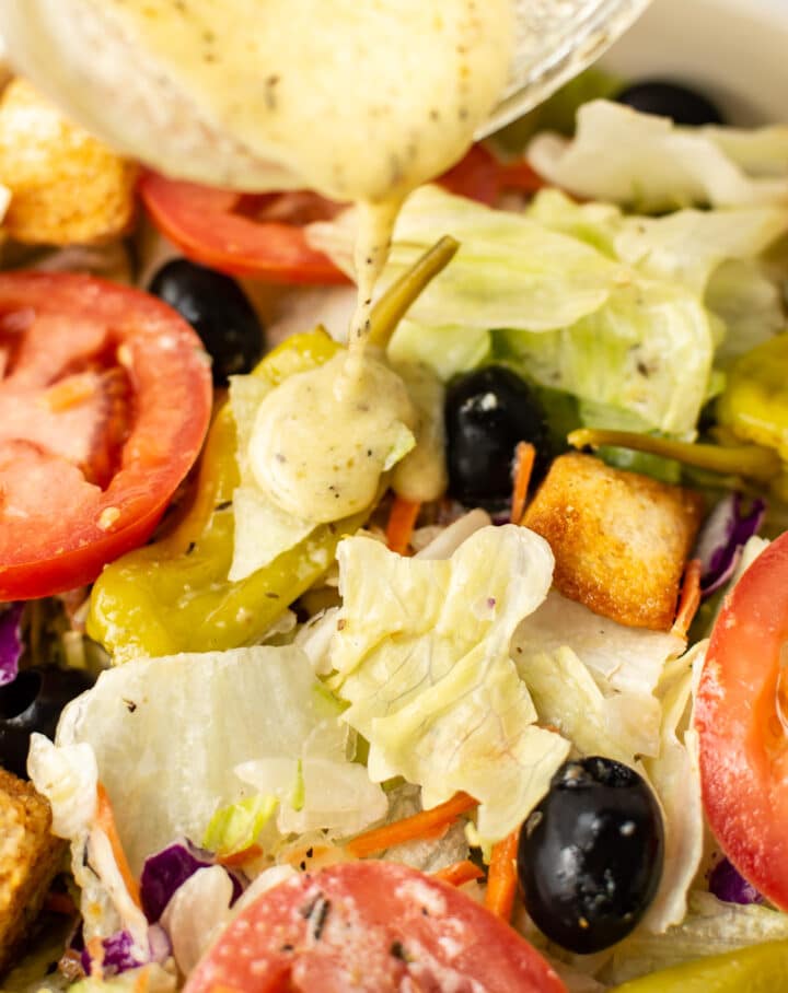 close up of a salad with italian dressing being drizzled