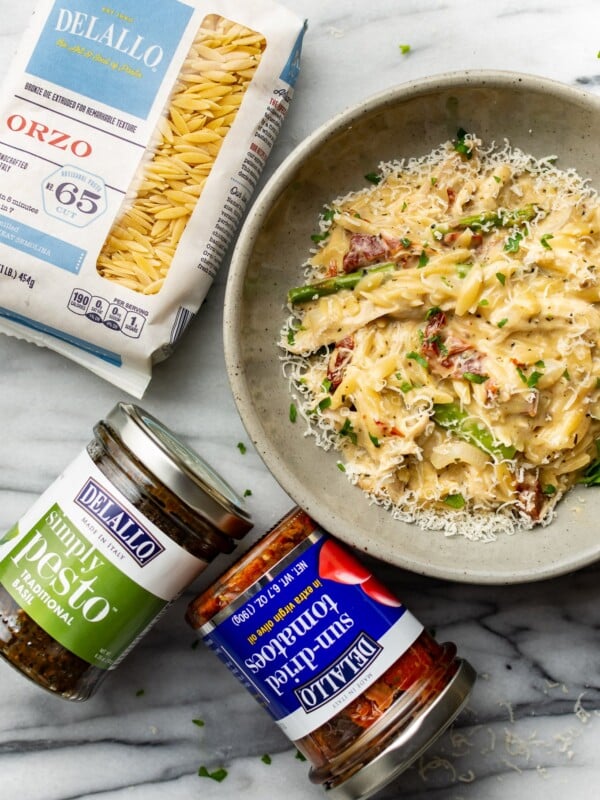 a bowl of pesto orzo next to delallo products