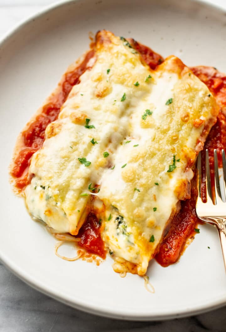 a portion of cheesy manicotti on a plate with a fork