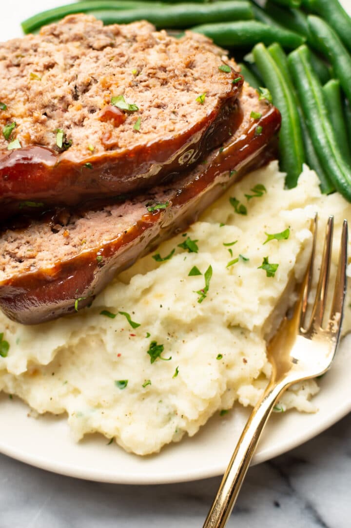 a plate with meatloaf, mashed potatoes, green beans, and a fork