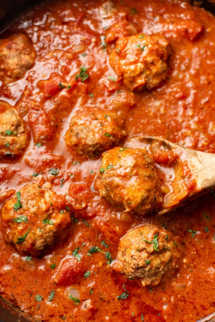 closeup of a wooden spoon with a meatball in tomato sauce